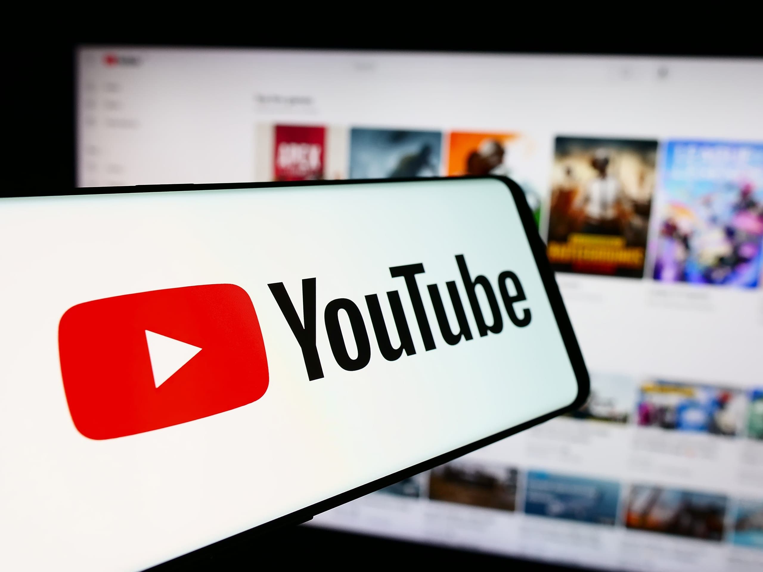 YouTube image on a phone in front of the YouTube homepage on a desktop